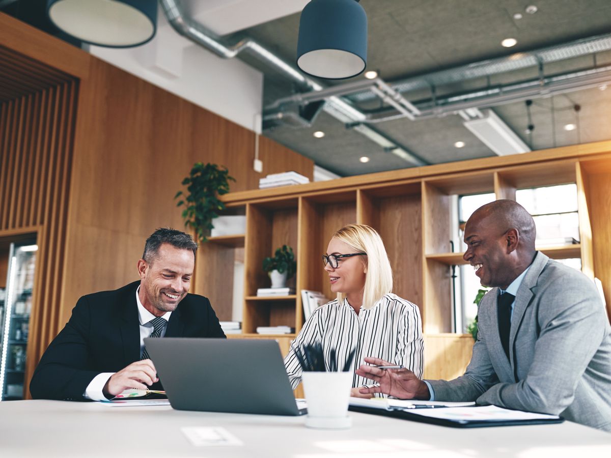 Three JEM team members laughing while working together at a shared desk